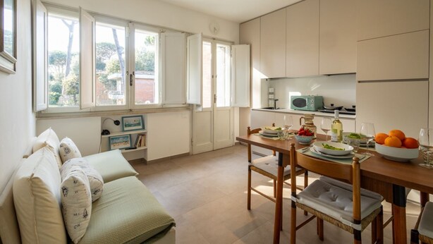 Eine moderne Küche mit Esstisch, Stühlen und Blick auf den Garten durch große Fenster.