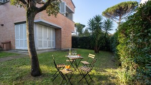 Eine Terrasse mit Tisch und Stühlen, ein Baum und ein Backsteinhaus im Hintergrund.
