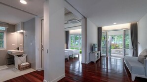 Ein modernes Hotelzimmer mit Holzboden, einem Balkon mit Vorhängen, einem Bett, einem Fernseher und einem Badezimmer mit Waschbecken und Dusche.