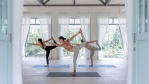 Ein geräumiger Raum mit großen Fenstern, einer hohen Decke mit freiliegenden Balken und Yogamatten auf dem Boden.