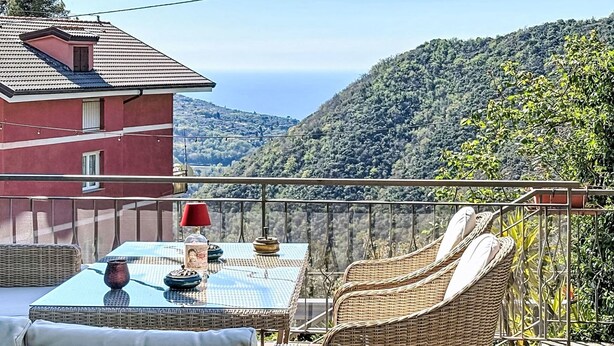 A balcony with wicker furniture, a table with a glass top, and a view of a mountainous landscape. - Vacation home Canepa by Interhome (Sori)