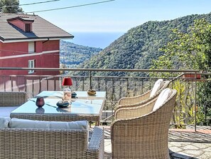 A balcony with wicker furniture, a table with a glass top, and a view of a mountainous landscape. - Vacation home Canepa by Interhome (Sori)