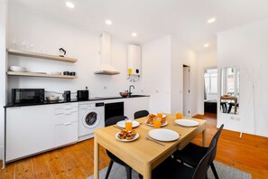 A modern kitchen with a dining area, white cabinetry, a washing machine, and a dining table set for breakfast. - Discover Lisbon from São Vicente Base (Lisbon)