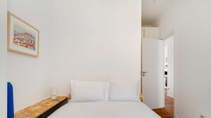 Ett hotellrum med en säng, ett nattduksbord, en lampa och en inramad tavla på väggen.