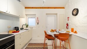 Une cuisine moderne avec des meubles blancs, une cuisinière noire et un coin repas avec des chaises orange et une table blanche.
