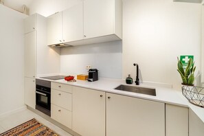 A modern kitchen with white cabinets, a stainless steel sink, and a built-in oven. - Douro Prestige Studio w/ Private Sunny Backyard (Porto)