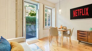 Quarto com uma mesa de jantar, cadeiras, um sofá, uma TV fixada na parede e uma porta que dá para uma área externa.
