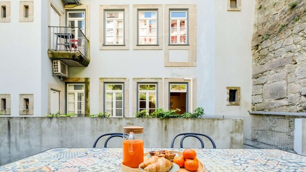 Uma mesa com itens de café da manhã, uma varanda e um edifício com várias janelas e uma parede de pedra.