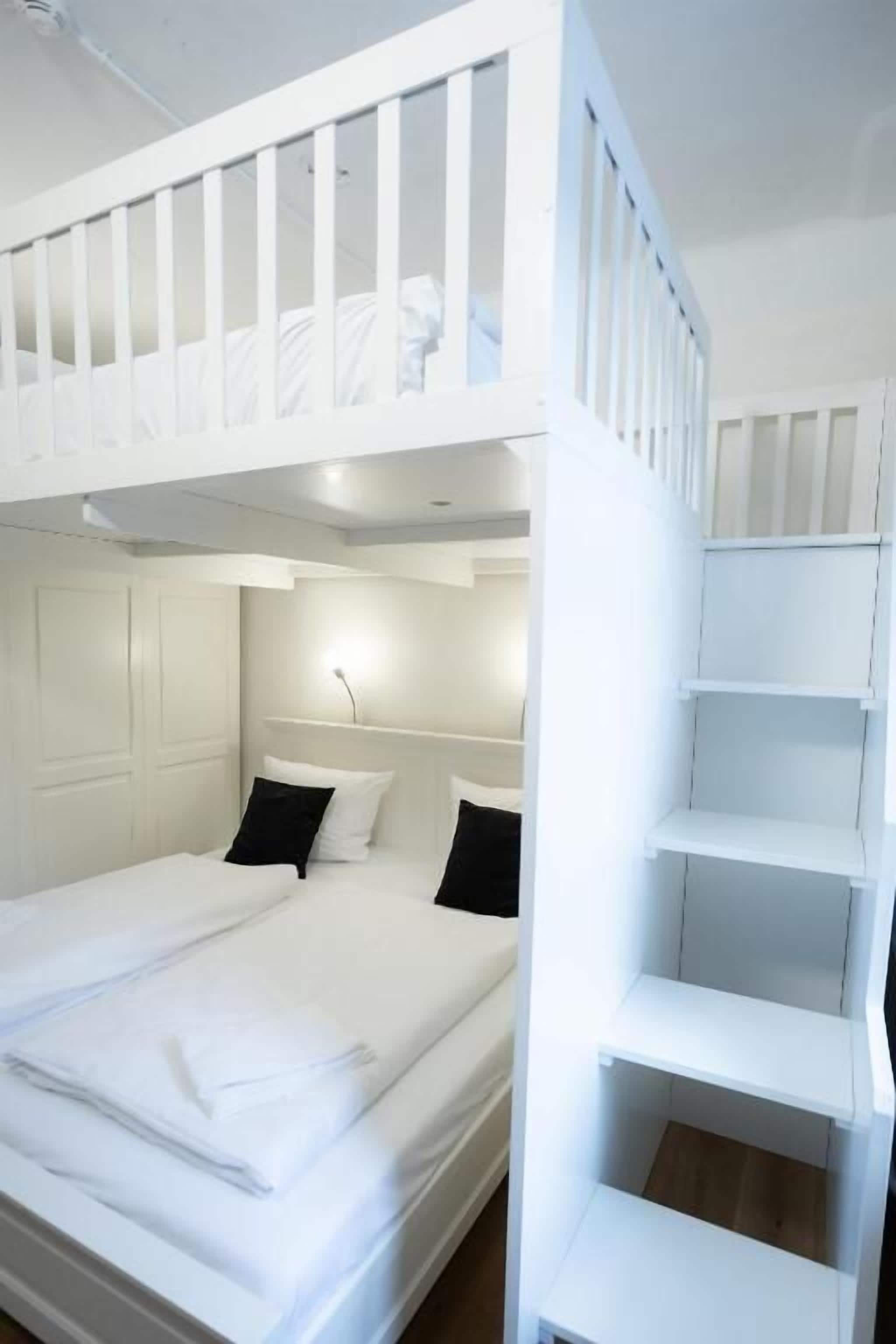 A bunk bed with a white railing, a bedside table with a lamp, and a white wardrobe.