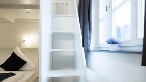 A room with a white staircase, a white radiator, a window with curtains, and a white sofa with a black pillow. - heimatgleis (Brilon)