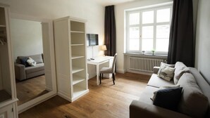 A room with a white desk, a chair, a sofa, a TV, and a window with curtains. - heimatgleis (Brilon)