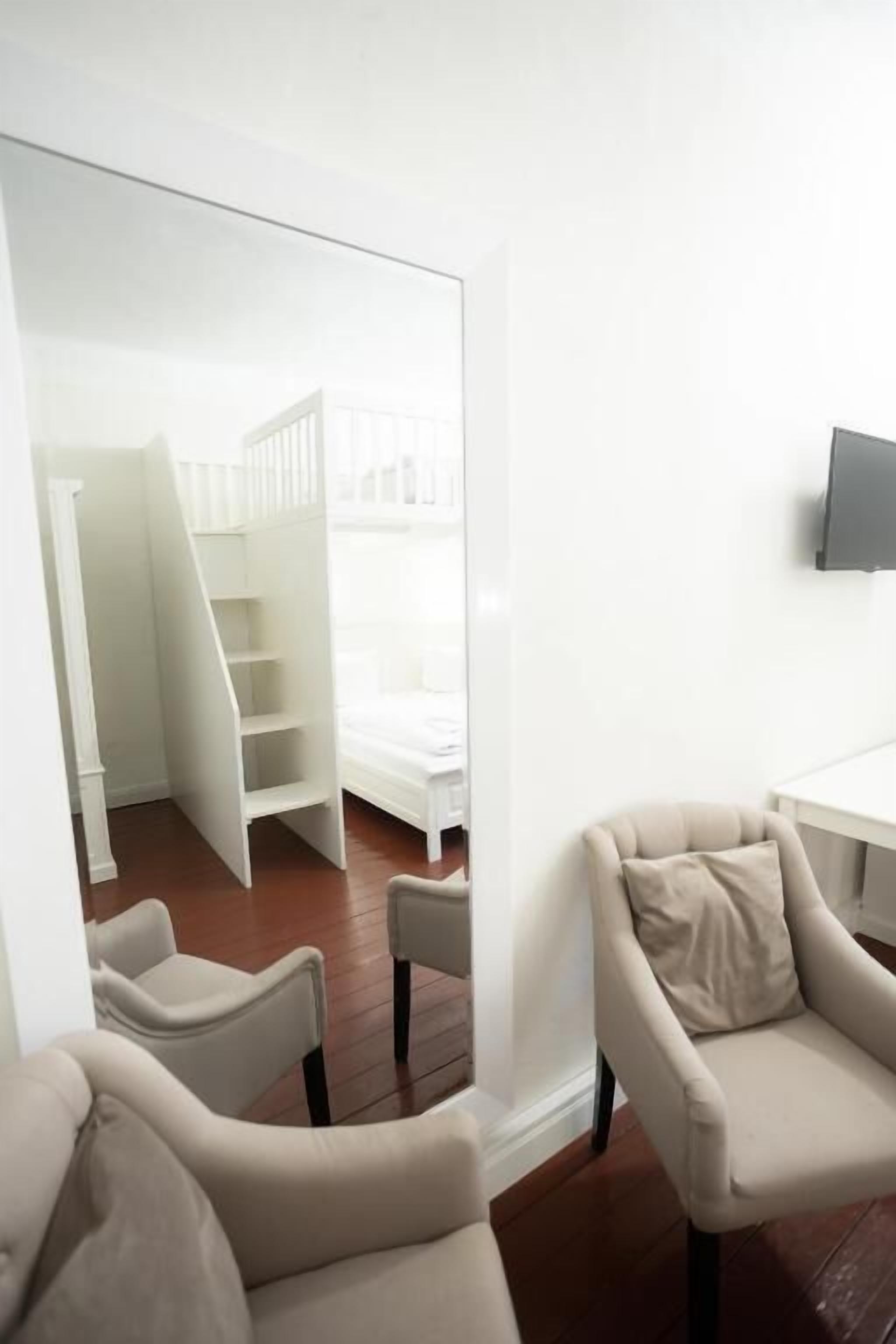 A room with a white bed, a TV on the wall, and a staircase leading to a loft.