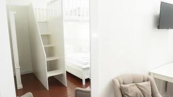 A room with a white bed, a TV on the wall, and a staircase leading to a loft.