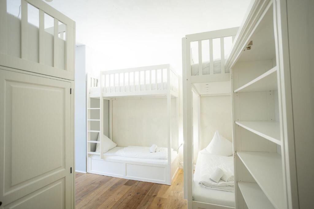 Una habitación con literas, suelo de madera y paredes blancas.