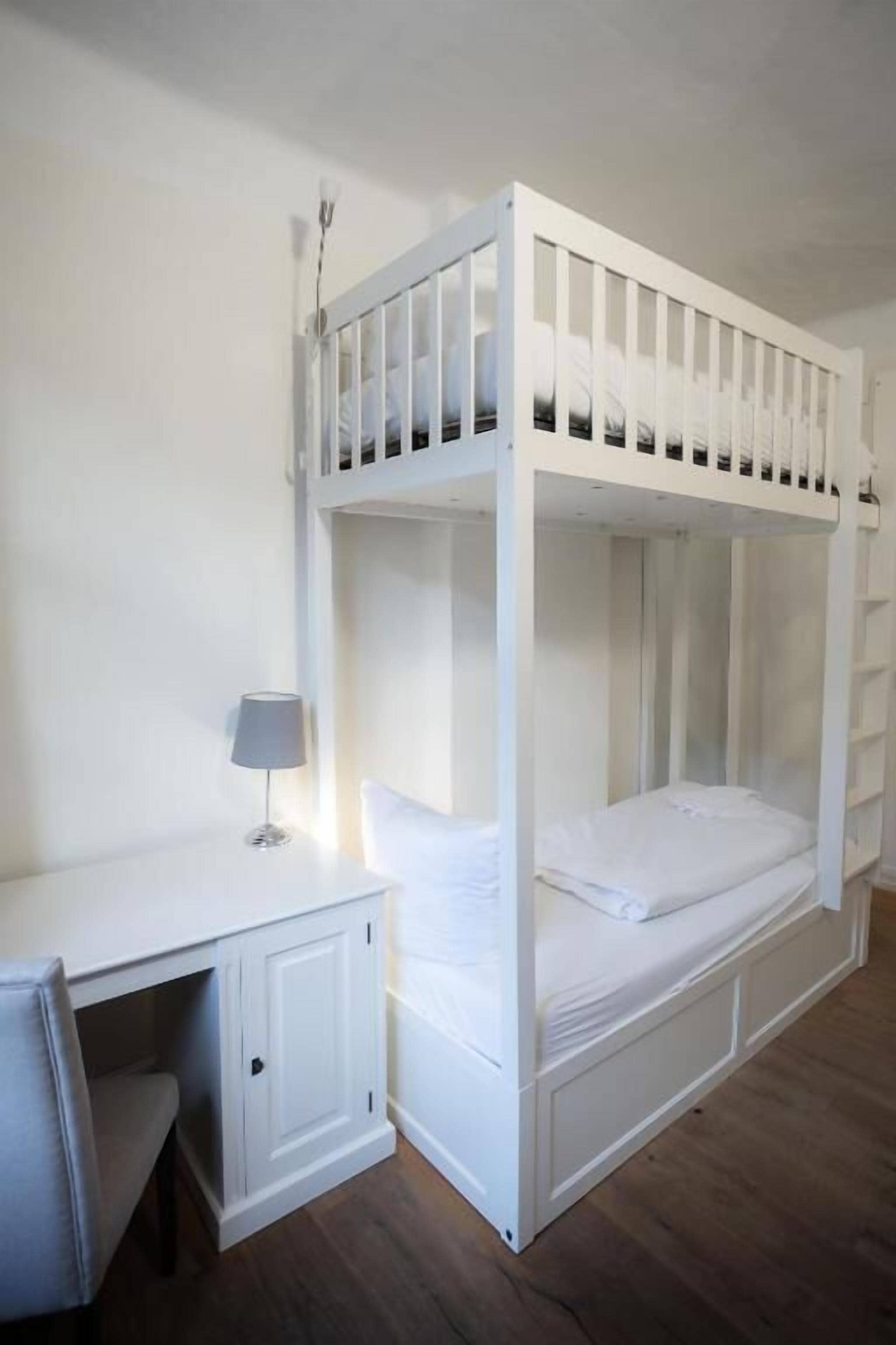 A bunk bed with a desk and chair, a lamp, and a white wardrobe.