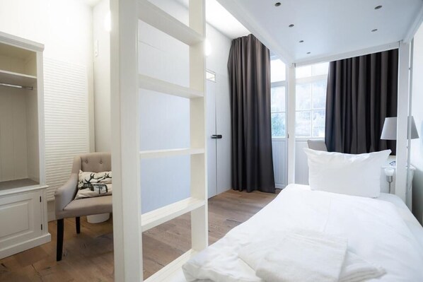 A hotel room with a bed, a chair, a wardrobe, and a window with curtains. - heimatgleis (Brilon)