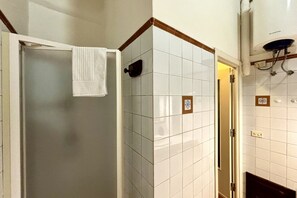 A bathroom with white tiled walls, a glass shower enclosure, and a towel hanging on the door. - Vintage Flat - Elegance and Charm in the Heart of Cagliari (Cagliari)