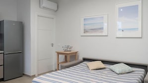 Ein Schlafzimmer mit einem Bett, einem kleinen Tisch, einem Kühlschrank und zwei gerahmten Bildern an der Wand.