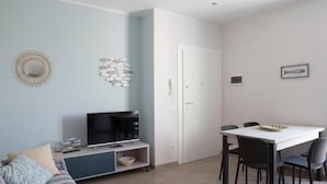 Ein modernes Wohnzimmer mit Sofa, Fernseher, Esstisch und Stühlen.