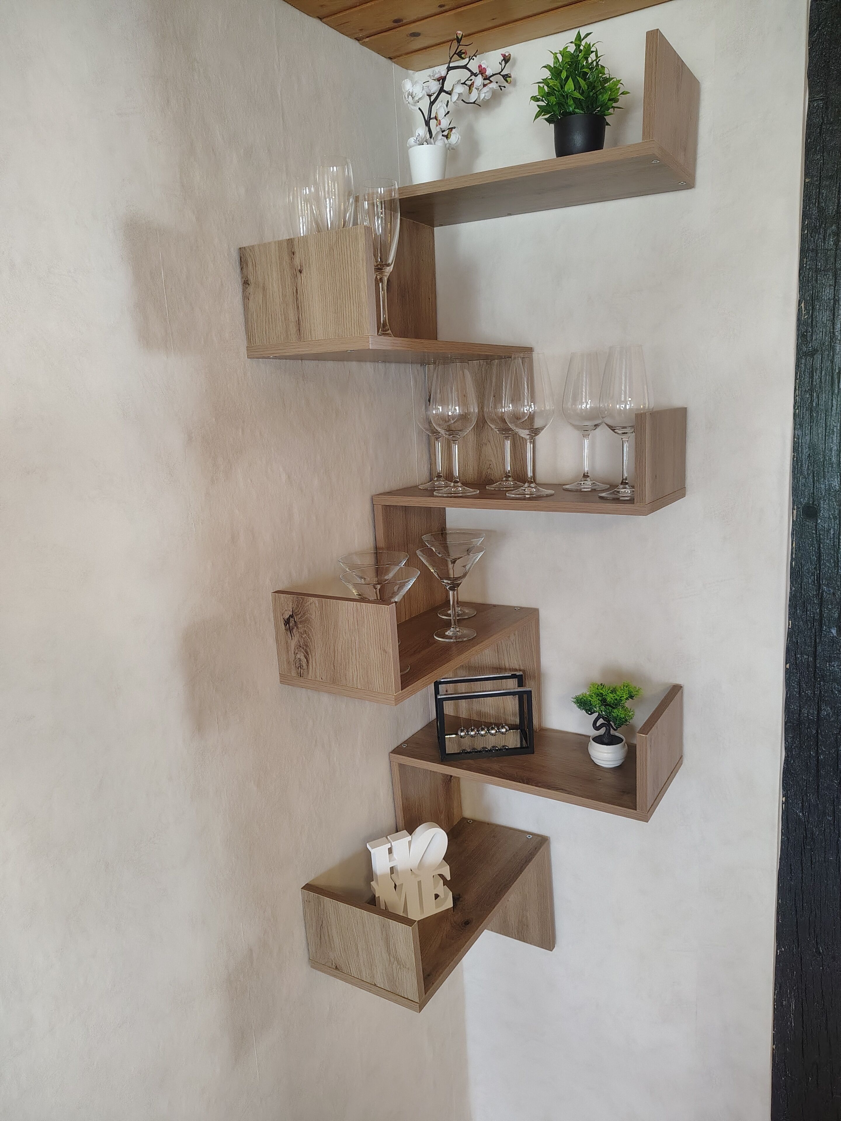 Un'unità a scaffali in legno fissata al muro, con bicchieri, una pianta in vaso e un piccolo bonsai.