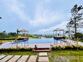 A swimming pool with two gazebos, surrounded by greenery and a distant view of houses.