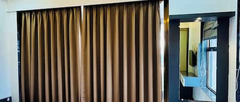 A hotel room with a bed, a desk with a mirror, and curtains.