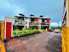 A multi-story residential building with a green lawn, a red door, and a parked car.