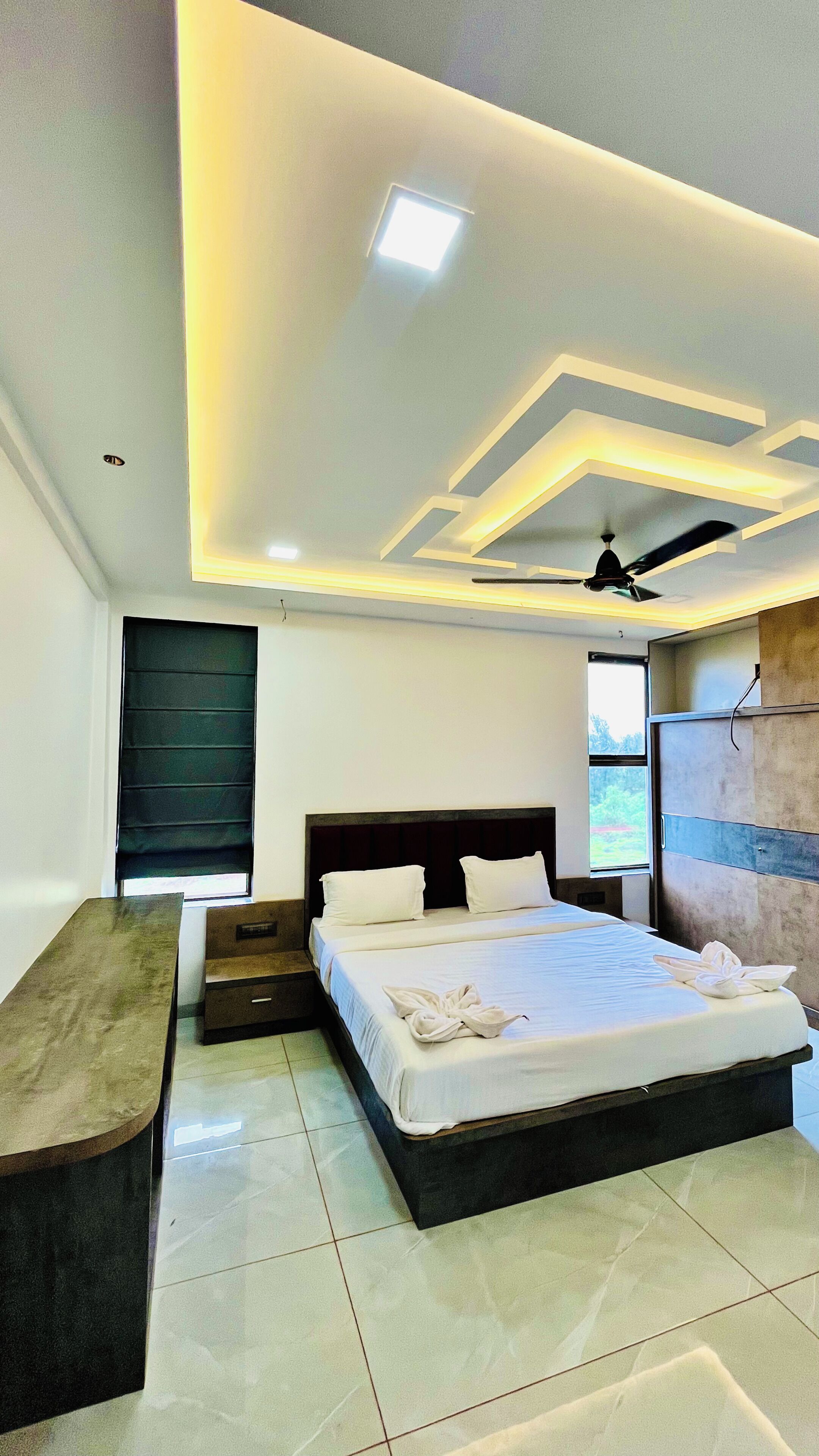 A modern bedroom with a bed, bedside tables, a bench, a ceiling fan, and a window.