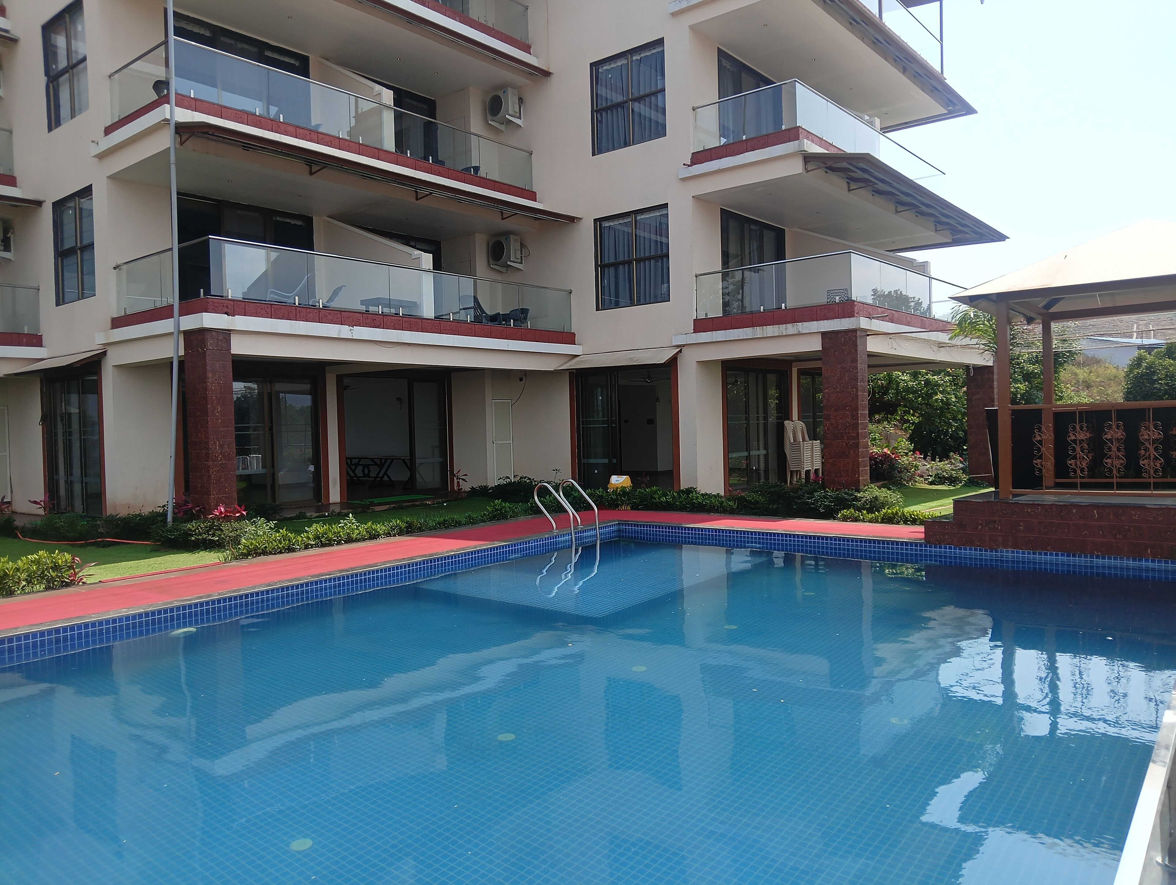 A multi-story hotel with a swimming pool, balconies, and a covered outdoor area.