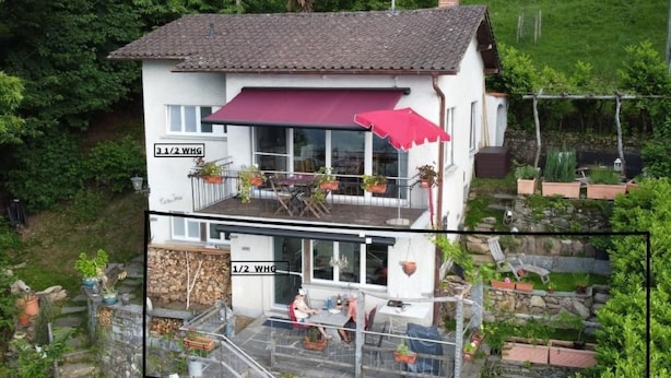 A two-story house with a red awning, outdoor seating, and potted plants. - Casa Ines - 1 1/2 Zimmer Whg Terrasse mit Seesic by Interhome (Magadino)