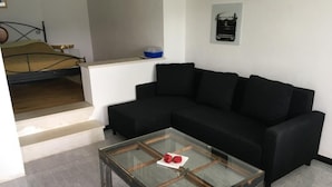 A living room with a black sofa, a glass coffee table, and a bed with a wooden headboard. - Casa Ines - 1 1/2 Zimmer Whg Terrasse mit Seesic by Interhome (Magadino)