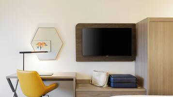 Una habitación de hotel con escritorio, una silla amarilla, televisión, cama y armario.