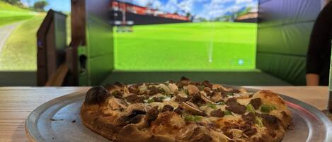 A pizza on a metal tray with a golf course projection in the background.