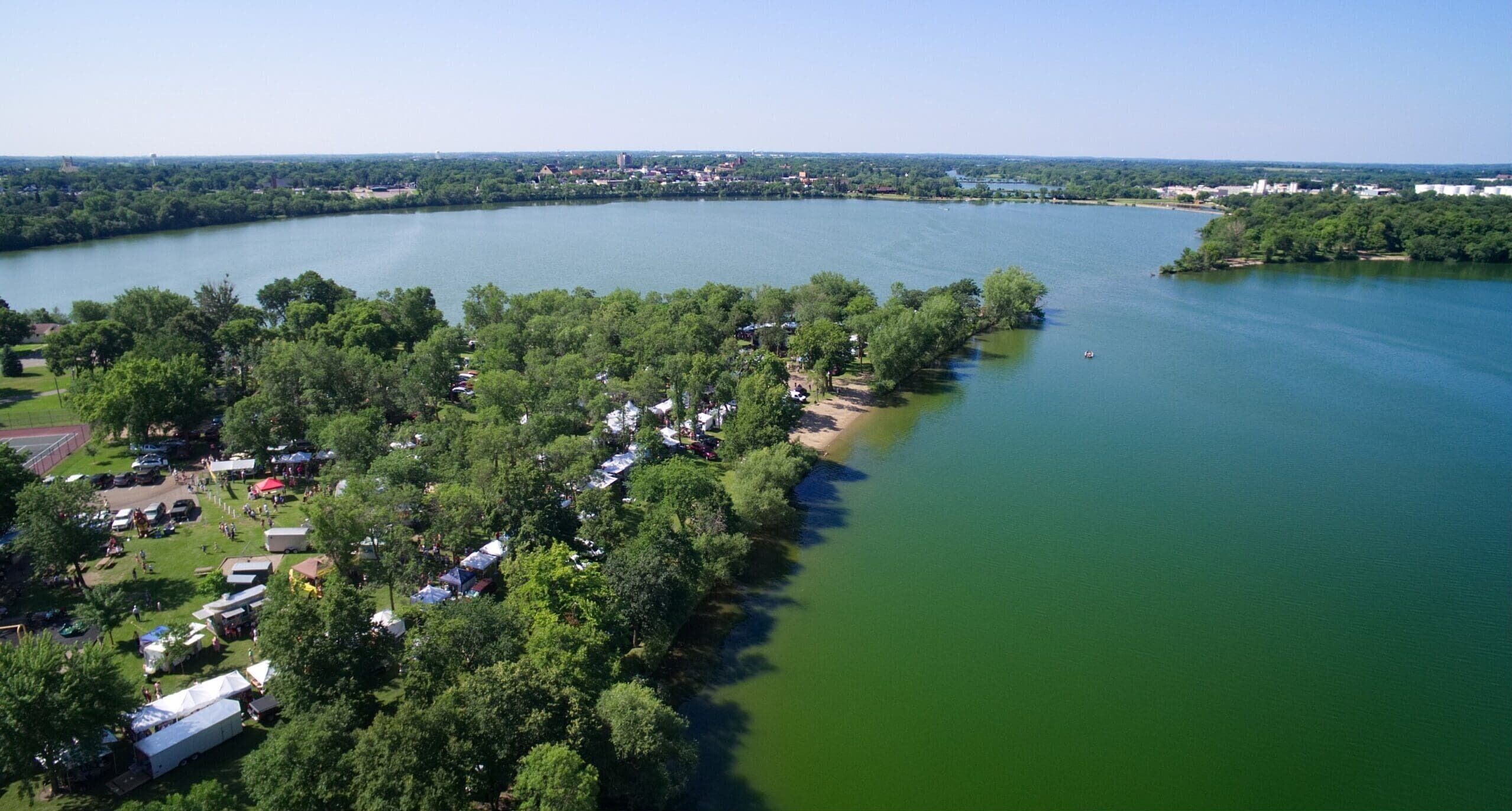 Luchtbeeld van een rivierengebied met een rij campers en tenten langs het water.
