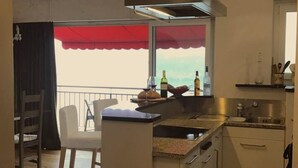 Une cuisine dotée d’un îlot central, un coin repas avec une chaise, un lustre et une vue par la fenêtre.