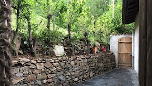 Un mur de pierres avec une porte en bois, un chemin de pierres et de la verdure.