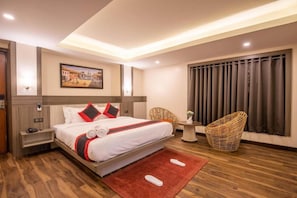 Una habitación de hotel con una cama grande, una mesita, una silla y una ventana con cortinas.