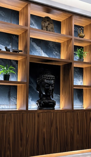 Una estantería de madera con una estatua de Buda en el centro, rodeada de varios objetos decorativos.
