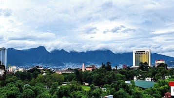 A cityscape with buildings, a mountain range, and a cloudy sky.
