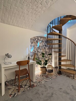Ein modernes Zimmer mit einer Wendeltreppe, einem Schreibtisch mit Stuhl, einer Topfpflanze und einer Wand mit Muster.