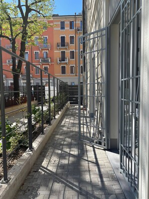 Ein gepflasterter Weg mit Metallgeländern, ein von Bäumen gesäumter Pfad und ein Gebäude mit großen Fenstern und Balkonen.