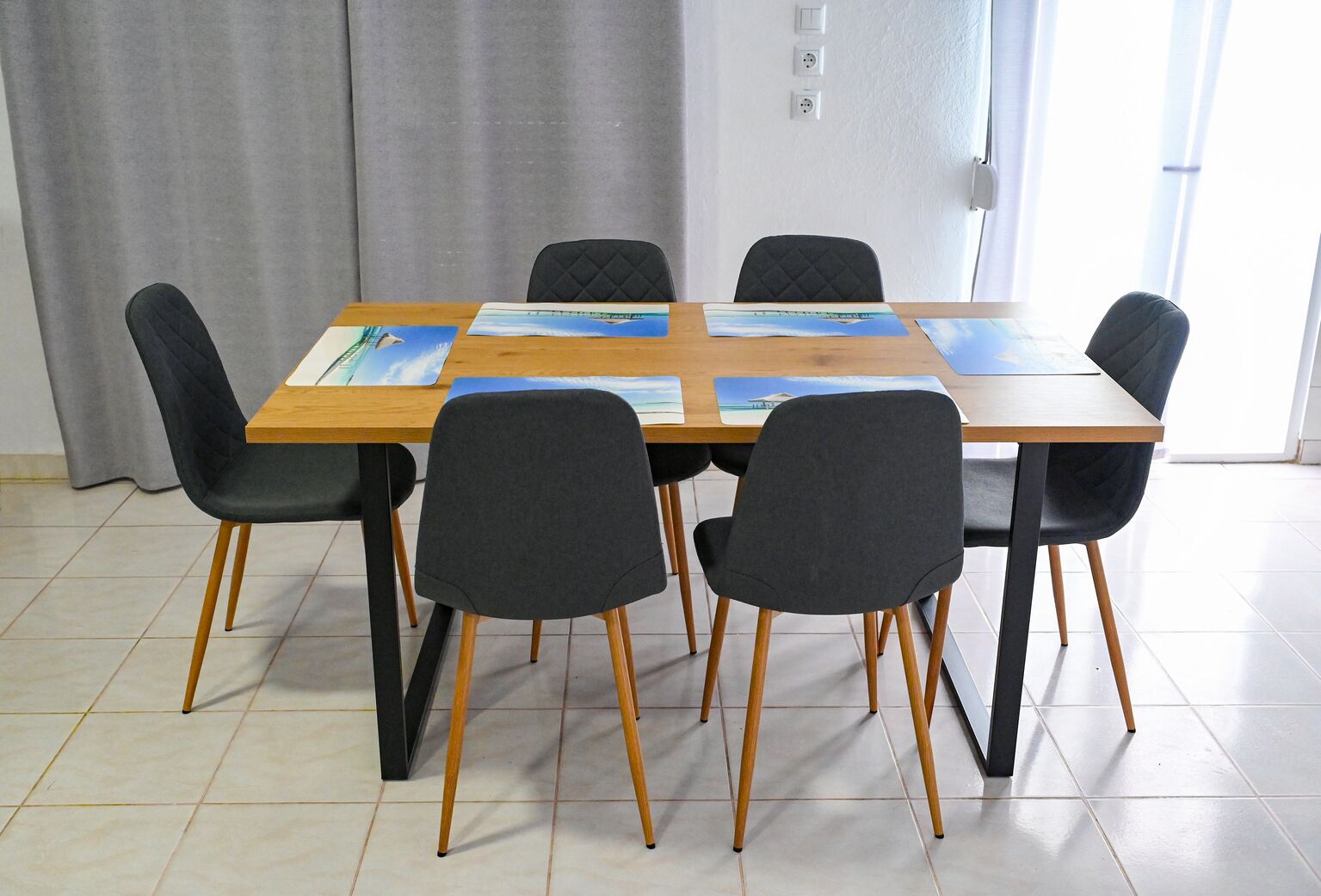 Zona pranzo con tavolo in legno e sei sedie nere, ognuna con gambe in legno.