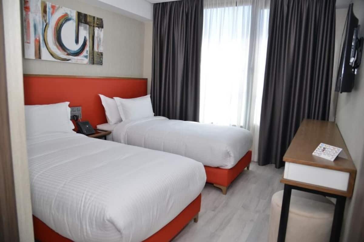 A hotel room with two beds, a desk, a chair, a TV, and a painting on the wall.