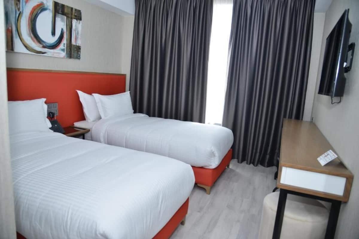 A hotel room with two beds, a desk, a TV, and a painting on the wall.
