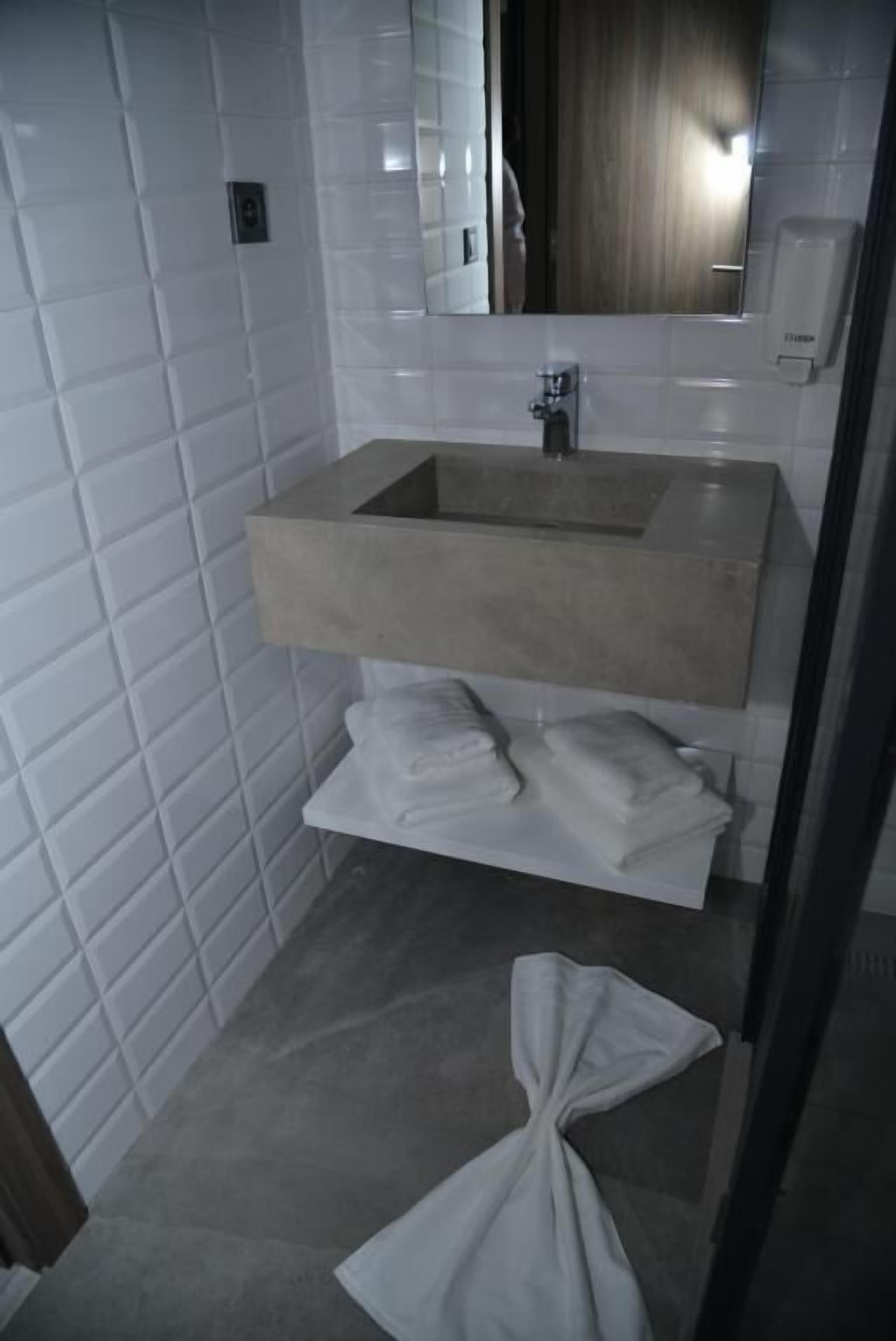 A bathroom with white tiled walls, a beige sink, and a mirror above it.