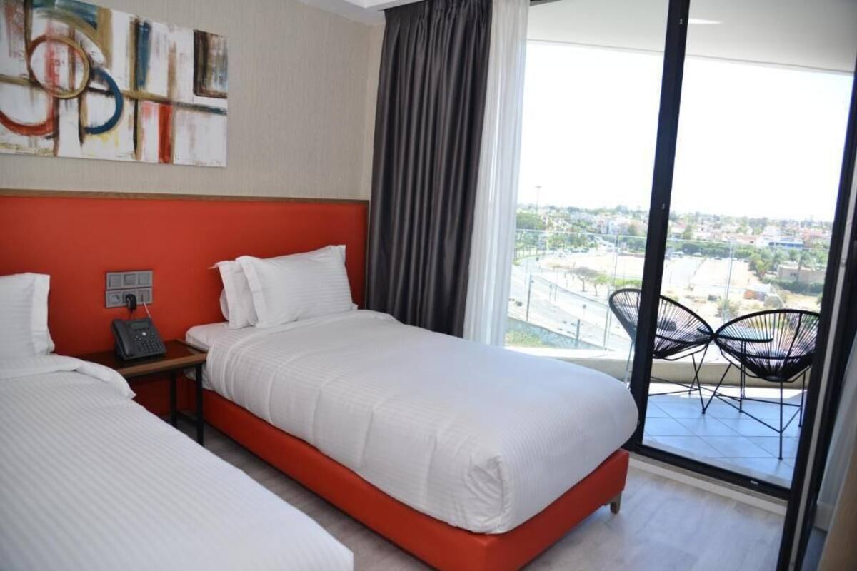 A hotel room with two beds, a large window with a view, and a balcony with chairs.