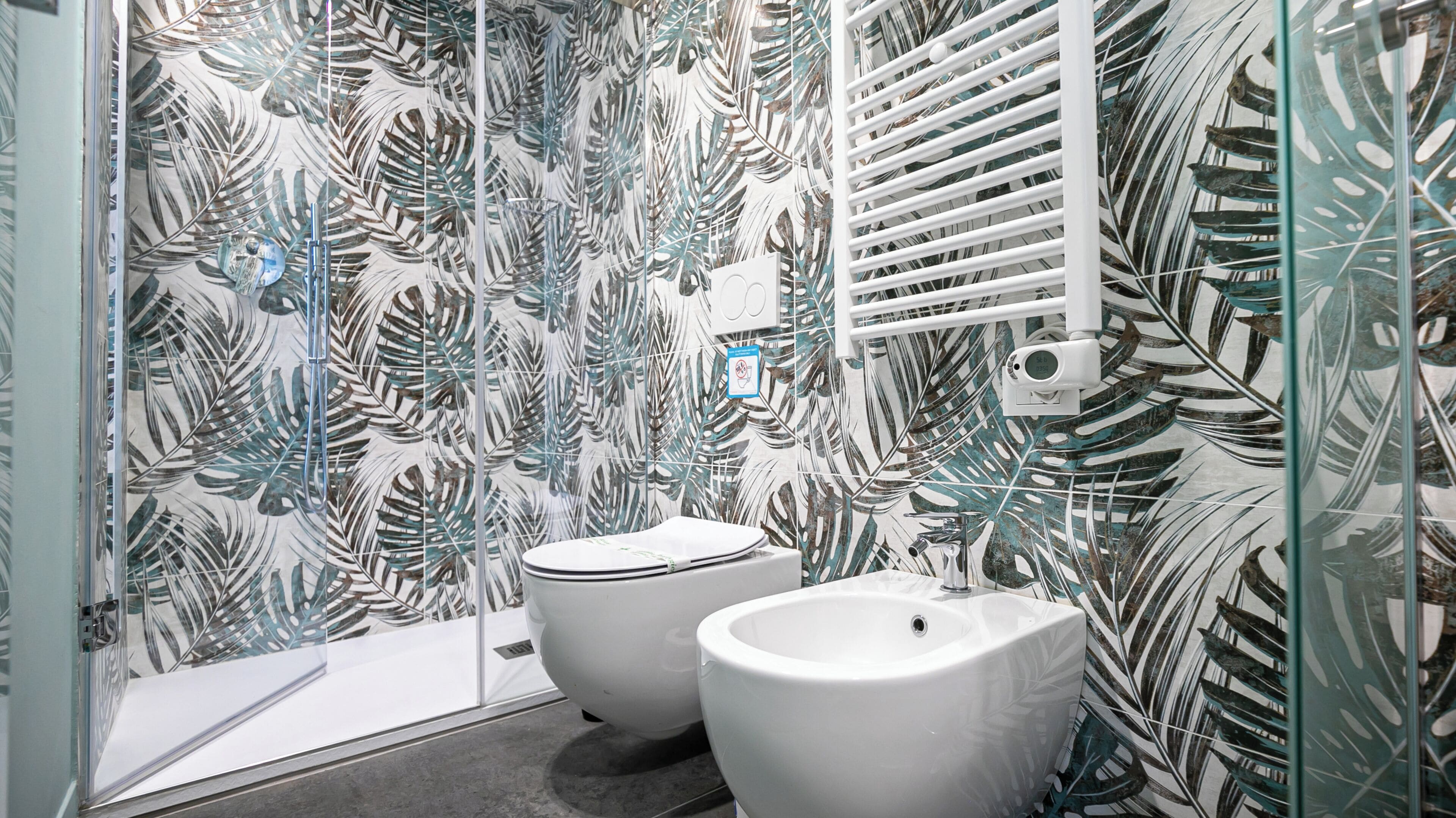 A bathroom with a leaf-patterned wall, a toilet, and a bidet.