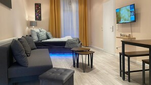 Een moderne woonkamer met een bank, voetenbankje, een klein tafeltje en een aan de muur bevestigde televisie.