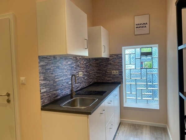 A modern kitchen with a stone backsplash, a stainless steel sink, and white cabinetry. - Apartment Sleeps 3 With Parking and Garden (Koblenz)