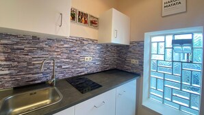 Een keuken met een betegelde achterwand, witte kasten, een roestvrijstalen spoelbak en een raam met geëtste glas.